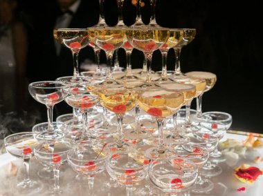 Champagne glasses standing in a tower at the wedding party. Champagne glass pyramid. Pyramid of glasses of wine, champagne, tower of champagne. Wedding party at night