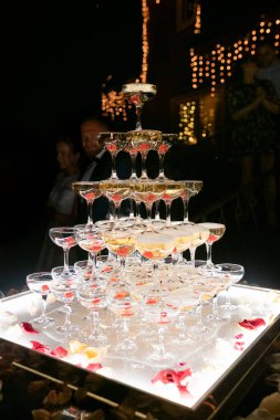 Champagne glasses standing in a tower at the wedding party. Champagne glass pyramid. Pyramid of glasses of wine, champagne, tower of champagne. Wedding party at night