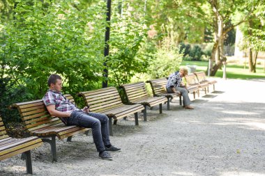 VILNIUS, LITHUANIA - 31 AĞUSTOS 2017: Litvanya, Vilnius 'taki Kamu Parkı. Genç çocuk bankta oturuyor ve cep telefonuna bakıyor.