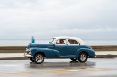 HAVANA, CUBA - 21 Ekim 2017: Havana, Küba 'daki eski araba. Retro Araç genellikle yerel halk ve turistler için bir taksi olarak kullanılır. Arka planda Karayip Denizi. Panning Mavi Renkli Araba