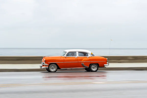 stock image HAVANA, CUBA - OCTOBER 21, 2017: Old Car in Havana, Cuba. Pannnig. Retro Vehicle Usually Using As A Taxi For Local People and Tourist. Caribbean Sea in Background. Orange Color
