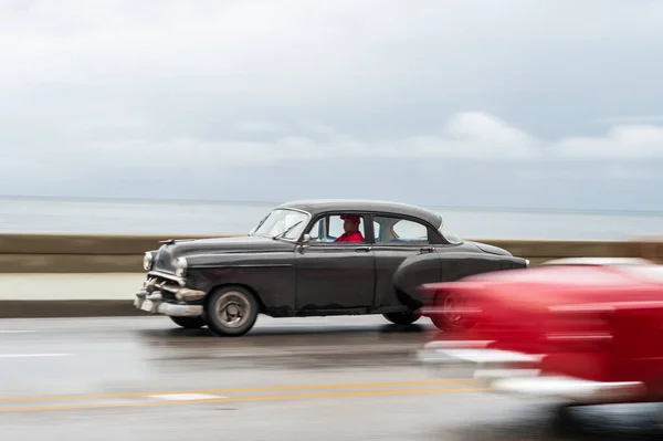 stock image HAVANA, CUBA - OCTOBER 21, 2017: Old Car in Havana, Cuba. Retro Vehicle Usually Using As A Taxi For Local People and Tourist. Caribbean Sea in Background. Panning Black Color Car