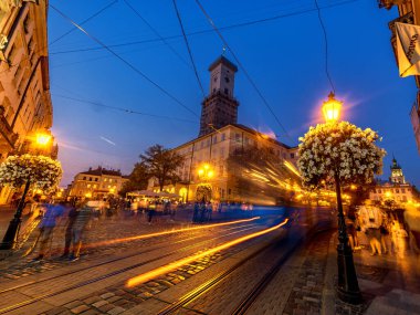 LVIV, UKRAINE - 12 Eylül 2016: Lviv City ve Lviv Old Town With People. Sunset Light ve Lviv City Hall with Moving Tram. Uzun Maruz Kalmaktan Bulanık İnsanlar.