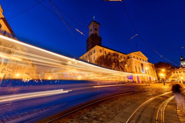LVIV, UKRAINE - 12 Eylül 2016: Lviv City ve Lviv Old Town With People. Sunset Light ve Lviv City Hall with Moving Tram. Uzun Maruz Kalmaktan Bulanık İnsanlar.