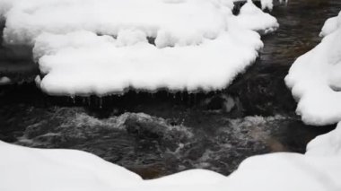 Bir nehrin kış manzarası, su yavaşça nehirden aşağı akıyor. Nehirde eriyen buzlar. Litvanya. Yavaş Hareket
