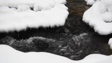 Bir nehrin kış manzarası, su yavaşça nehirden aşağı akıyor. Nehirde eriyen buzlar. Litvanya. Yavaş Hareket