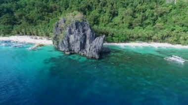 Palawan 'da Yedi Komando ve Papaya Sahili, Manzara Mekanı. El Nido, Filipinler 'de A turu. Berrak turkuaz suyu olan sakin, beyaz kumlu plaj, arka planda palmiye ağaçları, kaya oluşumları. İHA