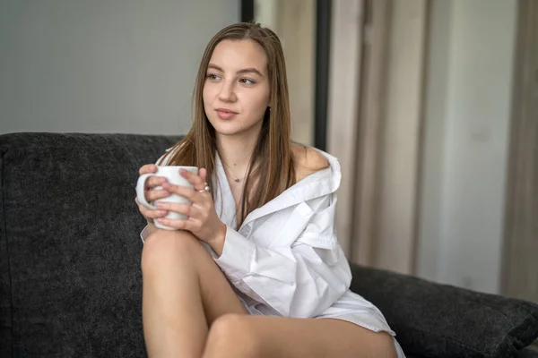 Piękna Młoda Dziewczyna Siedzi Kanapie Salonie Picia Kawy Białych Koszulach — Zdjęcie stockowe