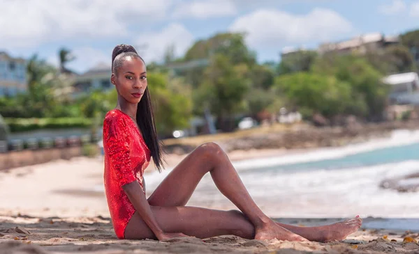 stock image Portrait of Beautiful Caribbean Adult Teen in Barbados. Wearing Red Bikini and Sitting on a tropical beach. Caribbean Sea in Background. Black. Portrait.