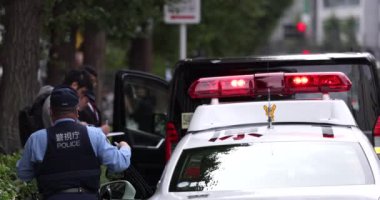 Arka planda polis arabası ve polis var. Kırmızı ışık. Tokyo, Japonya. Trafik kurallarını çiğneyen iki polis memuru.