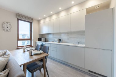 Klasik Beyaz Mutfak İçi ve Yemek Masası. Fırın, çaydanlık, mikrodalga ve cam. Tabaklar masanın üzerinde. Asgari İç Tasarım.