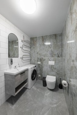 Parlak Zarif Modern Minimalist Banyo Beyaz Lavabolu Duş Odasının İç Tasarımı. Banyo aksesuarları, gri fayans duvarları, ayna, çamaşır makinesi ve musluk. LED Işık