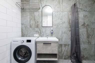 Parlak Zarif Modern Minimalist Banyo Beyaz Lavabolu Duş Odasının İç Tasarımı. Banyo aksesuarları, gri fayans duvarları, ayna, çamaşır makinesi ve musluk. LED Işık