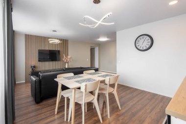 Modern Ev Oturma Odası ve Mutfak İçi. Lüks modern apartman dairesi. Açık Alan, Şık Siyah Deri Koltuk, Beyaz Mobilya, İskandinav Tasarımı. Duvarda Cllock, TV Ekranı