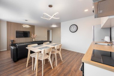 Modern Ev Oturma Odası ve Mutfak İçi. Lüks modern apartman dairesi. Açık Alan, Şık Siyah Deri Koltuk, Beyaz Mobilya, İskandinav Tasarımı. Duvarda Cllock, TV Ekranı