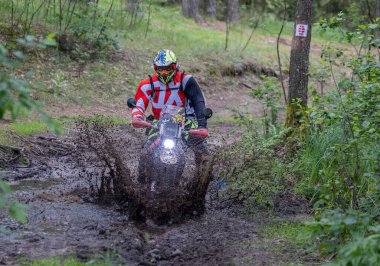 Moto ekipmanlı profesyonel motosikletçi doğada dayanıklı bisiklet sürüyor, sürücü çamurda ve su birikintilerinde sürüyor, motosiklet yarışı yapıyor. Off-road turnuvası. Ormanda dayanıklı sporlarda motosikletliler