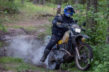 Moto ekipmanlı profesyonel motosikletçi doğada dayanıklı bisiklet sürüyor, sürücü çamurda ve su birikintilerinde sürüyor, motosiklet yarışı yapıyor. Off-road turnuvası. Ormanda dayanıklı sporlarda motosikletliler
