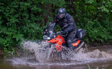 Moto ekipmanlı profesyonel motosikletçi doğada dayanıklı bisiklet sürüyor, sürücü çamurda ve su birikintilerinde sürüyor, motosiklet yarışı yapıyor. Off-road turnuvası. Ormanda dayanıklı sporlarda motosikletliler