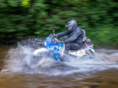 Moto ekipmanlı profesyonel motosikletçi doğada dayanıklı bisiklet sürüyor, sürücü çamurda ve su birikintilerinde sürüyor, motosiklet yarışı yapıyor. Off-road turnuvası. Ormanda dayanıklı sporlarda motosikletliler