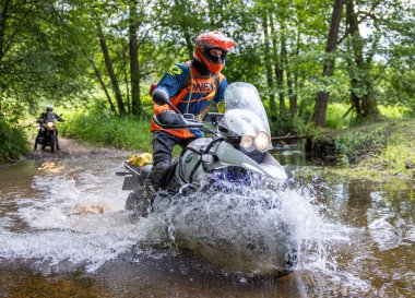 Moto ekipmanlı profesyonel motosikletçi doğada dayanıklı bisiklet sürüyor, sürücü çamurda ve su birikintilerinde sürüyor, motosiklet yarışı yapıyor. Off-road turnuvası. Ormanda dayanıklı sporlarda motosikletliler