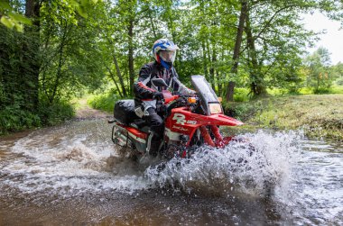 Moto ekipmanlı profesyonel motosikletçi doğada dayanıklı bisiklet sürüyor, sürücü çamurda ve su birikintilerinde sürüyor, motosiklet yarışı yapıyor. Off-road turnuvası. Ormanda dayanıklı sporlarda motosikletliler