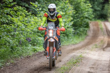 Moto ekipmanlı profesyonel bir motosikletçi. Doğada dayanıklı bisiklet sürüyor. Sürücü çakıllı yolda, motosiklet yarışında. Off-road turnuvası. Ormanda dayanıklı sporlarda motosikletliler