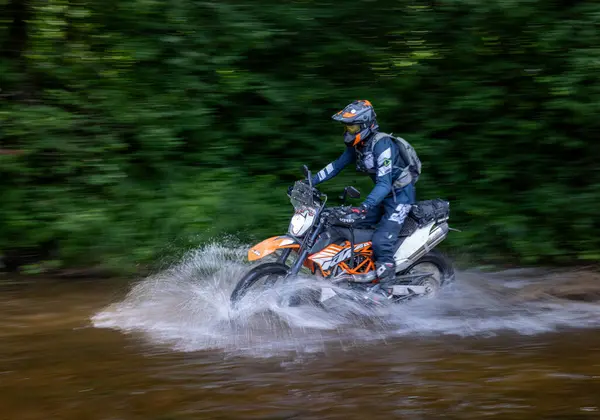 Moto ekipmanlı profesyonel motosikletçi doğada dayanıklı bisiklet sürüyor, sürücü çamurda ve su birikintilerinde sürüyor, motosiklet yarışı yapıyor. Off-road turnuvası. Ormanda dayanıklı sporlarda motosikletliler