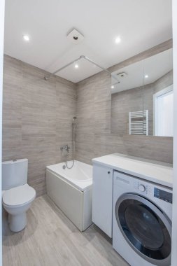 Parlak Zarif Modern Minimalist Banyo Duş Odasının İç Tasarımı. Banyo aksesuarları, gri fayans duvarları, ayna, çamaşırhane. LED Işık.