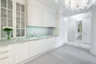 Lüks Konforlu Modern Açık Parlak Mutfak İçi. Arka planda musluk, çiçek, buzdolabı ve mobilya var. Gri renkli döşeme. Beyaz Dolaplar