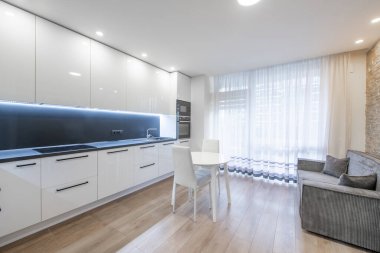 İskandinav Tarzı Konforlu Modern Açık Parlak Mutfak İç mimarisi. Fırın, Musluk, Buzdolabı, Mikrodalga. Beyaz renk. Yemek masası, ahşap zemin. Pencereler ve Perdeler. Koltuk, kanepe. Geniş Açı