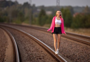 Güneş Gözlüğü Giyen Mutlu Kız Demiryolunda Yürüyor. Bulanık Arkaplan, Yumuşak Altın Saat Işığı