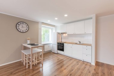 İskandinav tarzı rahat modern açık minimalizm mutfak iç mimarisi. Arka planda fırın, musluk, buzdolabı ve mobilya. Koyu Kahverengi Döşeme. Beyaz Dolaplar ve Duvardaki Saat. Geniş Açı