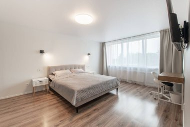 Lüks yatak odası, iç mekan, modern ev, güzel iç mekan, geniş yatak odası. Duvardaki TV seti. Büyük boy yatak, beyaz duvarlar ve tavan. Ahşap zemin. Geniş Açı