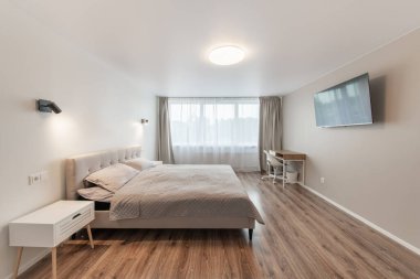 Lüks yatak odası, iç mekan, modern ev, güzel iç mekan, geniş yatak odası. Duvardaki TV seti. Büyük boy yatak, beyaz duvarlar ve tavan. Ahşap zemin. Geniş Açı