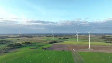 Rüzgar türbinlerinin hava görüntüleri zarifçe dönüyor ve daha fazla rüzgar türbini bulunuyor. Kıyıdaki ve tarımdaki sürdürülebilir sinerji. Güzel bir manzara. Altın Saat. 4k