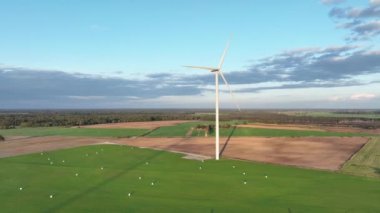 Rüzgar türbinlerinin hava görüntüleri zarifçe dönüyor ve daha fazla rüzgar türbini bulunuyor. Kıyıdaki ve tarımdaki sürdürülebilir sinerji. Güzel bir manzara. Altın Saat. 4k