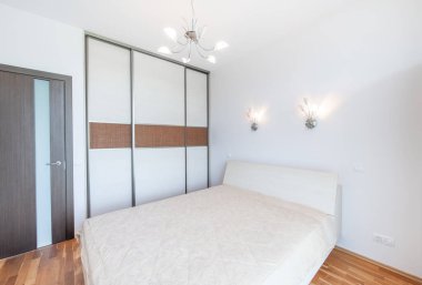 Geniş Ev Yatak Odası İçi Açısı. Arka planda büyük boy çift kişilik yatak ve gardırop. Beyaz Duvarlar. Aile Evi. Kapalı Tahta Kapı. Parlak Güneşli Gün