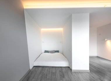 Minimalizm Ev Yatak Odası Apartmanı. Beyaz Parlak Duvarlar, Kara Ahşap Zemin. LED Lights Home Interior. Arka planda Açık Mutfak Bölgesi. İskandinav İç mimarisi. Geniş Açı