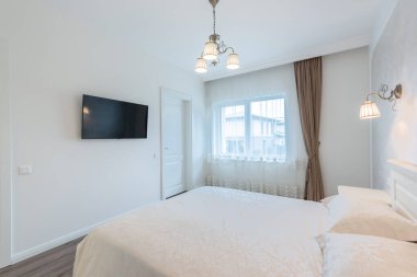 Lüks Ev Yatak Odası İçi. Büyük boy yatak, beyaz duvarlar ve tavan. Pencereler ve Perde. Kahve masası, yerde halı. LED Işık. Geniş Açı