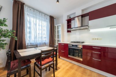 İskandinav Tarzı Konforlu Modern Mutfak Kırmızı ve Beyaz Dolaplar ve Yemek Alanı. İç mekan. Arka planda musluk, buzdolabı, fırın, dolap ve mobilya. Geniş Açı