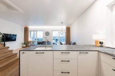 Modern Beyaz ve Gri Mutfak ve Şık Minimalist Tasarım. Ev Oturma Odası İçi Cam Yemek Masası ve Büyük Pencereli. Koltuk, arka planda kanepe. Geniş Açı