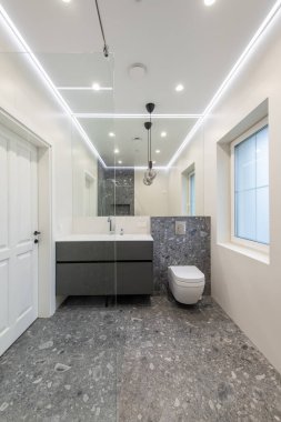 Gri fayans döşeme, minimalist gri kibir, beyaz duvarlar ve temiz ve şık bir görünüm için çevreye yayılmış aydınlatma içeren modern banyo.