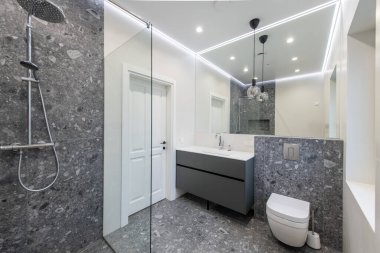 Gri fayans döşeme, minimalist gri kibir, beyaz duvarlar ve temiz ve şık bir görünüm için çevreye yayılmış aydınlatma içeren modern banyo.