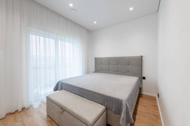 Çağdaş ev yatak odası, sade ama şık bir gri yatak takımı, modern tek kişilik yatak odası, katıksız perdelerin arasından doğal ışık, ve temiz ve rahatlatıcı bir ortam için hafif tonlarda duvarlar..