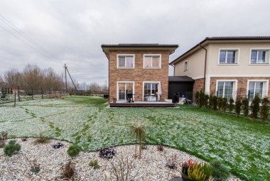 Avlusu ve garaj yolu olan tuğladan bir ev. Ev karla kaplı bir bahçeyle çevrilidir. Tuğla cepheli ve sıva kaplamalı iki katlı ev, karlı yeşil bir çimenlikle tamamlanmış.