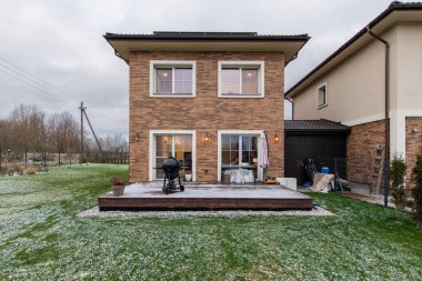 Avlusu ve garaj yolu olan tuğladan bir ev. Ev karla kaplı bir bahçeyle çevrilidir. Tuğla cepheli ve sıva kaplamalı iki katlı ev, karlı yeşil bir çimenlikle tamamlanmış.