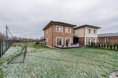 Avlusu ve garaj yolu olan tuğladan bir ev. Ev karla kaplı bir bahçeyle çevrilidir. Tuğla cepheli ve sıva kaplamalı iki katlı ev, karlı yeşil bir çimenlikle tamamlanmış.