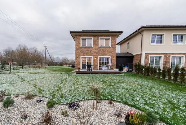 Avlusu ve garaj yolu olan tuğladan bir ev. Ev karla kaplı bir bahçeyle çevrilidir. Tuğla cepheli ve sıva kaplamalı iki katlı ev, karlı yeşil bir çimenlikle tamamlanmış.