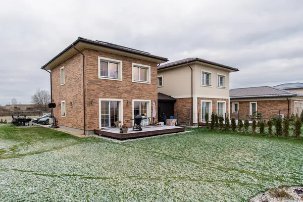 Avlusu ve garaj yolu olan tuğladan bir ev. Ev karla kaplı bir bahçeyle çevrilidir. Tuğla cepheli ve sıva kaplamalı iki katlı ev, karlı yeşil bir çimenlikle tamamlanmış.