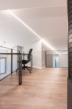 Modern ergonomik bir sandalye, büyük ahşap döşeme ve parlak minimalist tasarım elementleri içeren şık ofis odası, fonksiyonel çalışma ortamı arayan yaratıcı profesyoneller için mükemmel..